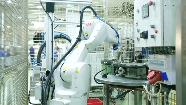 A white industrial robot moving between fixtures in a production cell.
